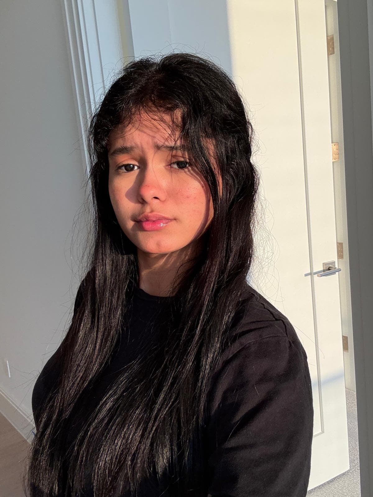 Young woman with long dark hair illuminated by golden sunlight, wearing a black shirt.
